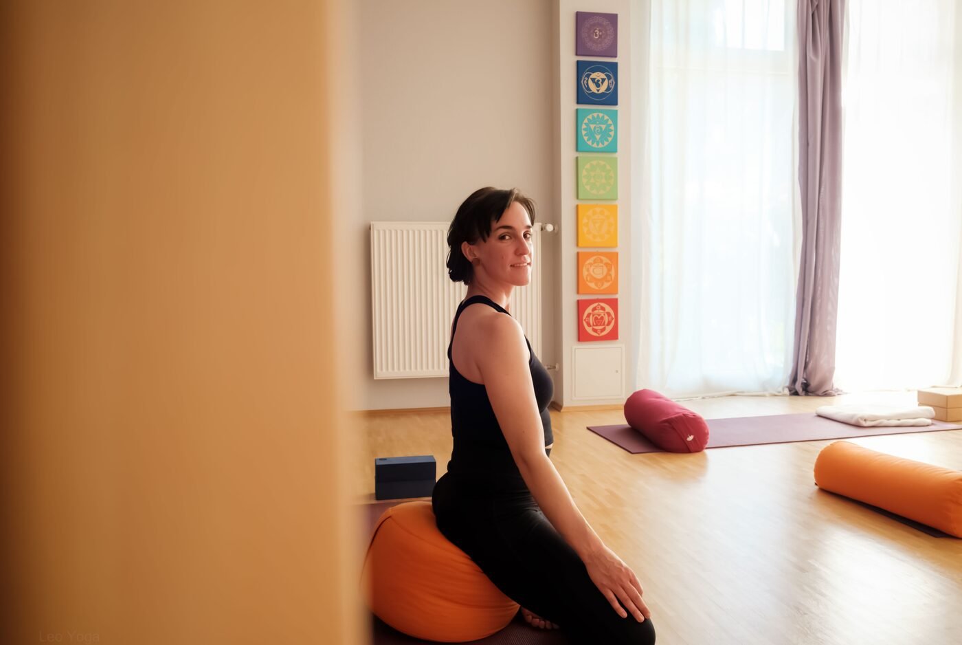 Leonie sitzt auf einem Kissen auf der Matte und schaut freundlich zur Kamera, im Seitenprofil.